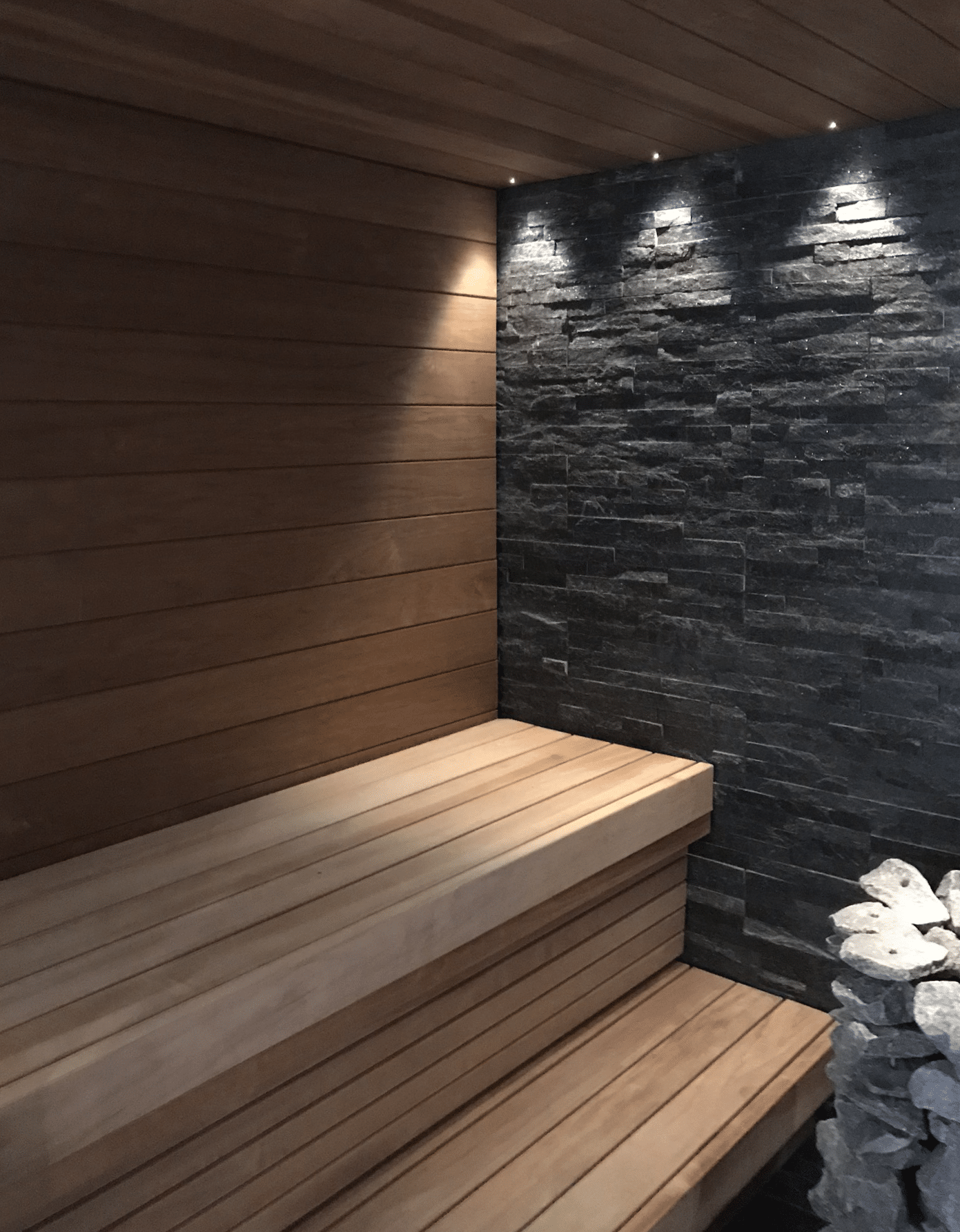 MRsauna-yksilolliset-uniikit-mittatilaussaunat-Uusimaa-Espoo Uusi sauna tunnelmallisessa valaistuksessa tummalla kiviseinalla.